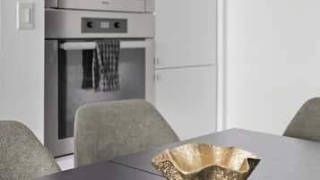 A modern kitchen with stainless steel appliances, a dining table with a unique gold bowl centerpiece, and grey upholstered chairs.