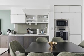 A modern kitchen with white cabinetry, a dining table with chairs, and built-in appliances including a microwave and oven. - Sleek Downtown Penthouse Apartment , Free Parking (Toronto)