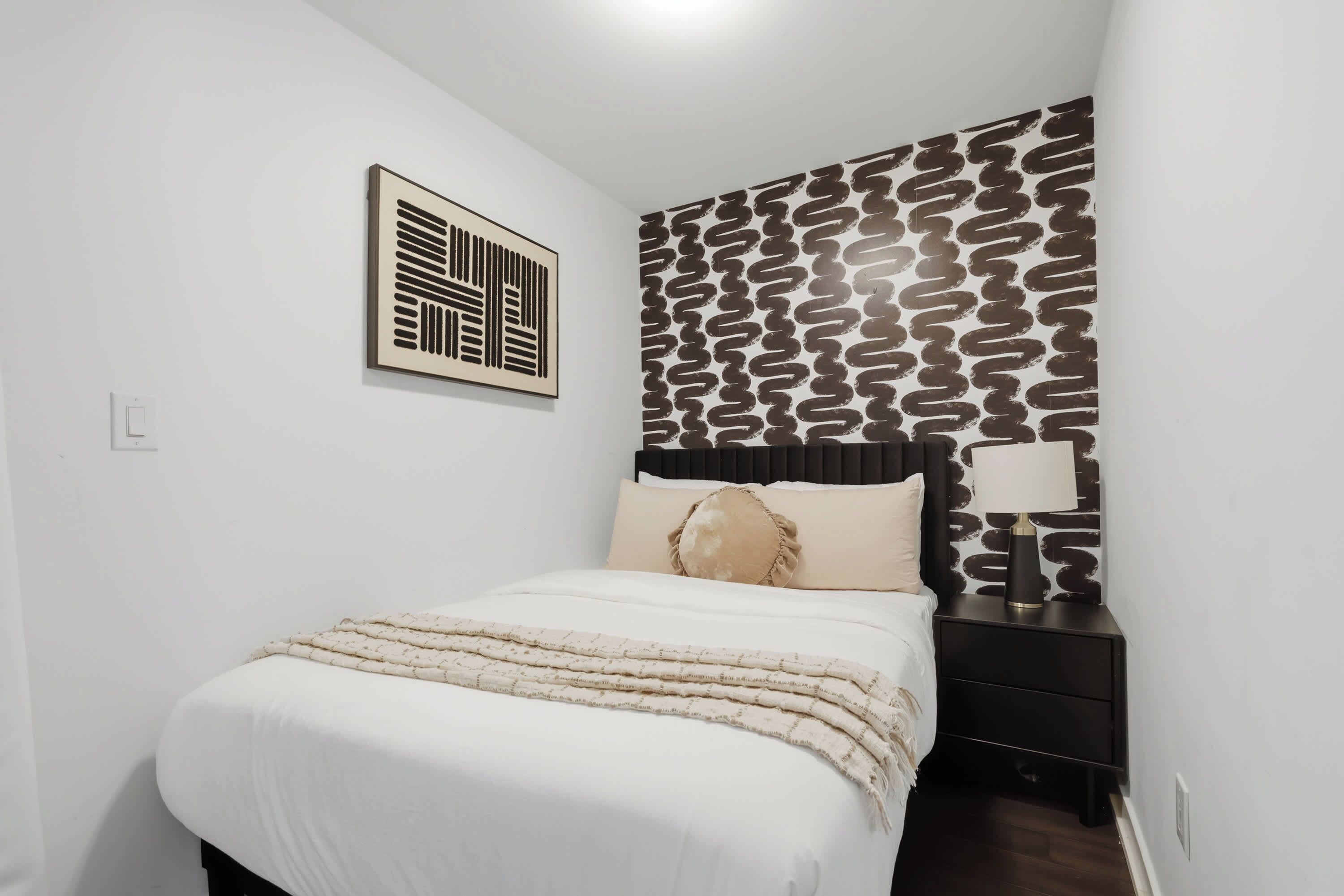 A bedroom with a bed, a nightstand, a lamp, and a patterned wall.