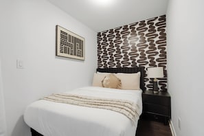 A bedroom with a bed, a nightstand, a lamp, and a patterned wall. - Sleek Downtown Penthouse Apartment , Free Parking (Toronto)