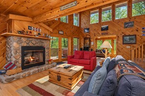 Interior de una cabaña con chimenea de piedra, paredes de madera, un sofá rojo, un sofá azul y una mesa de centro de madera.