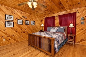 Ein Schlafzimmer mit Holzwänden, einem Bett, zwei Nachttischen, einem Deckenventilator und gerahmten Bildern an den Wänden.