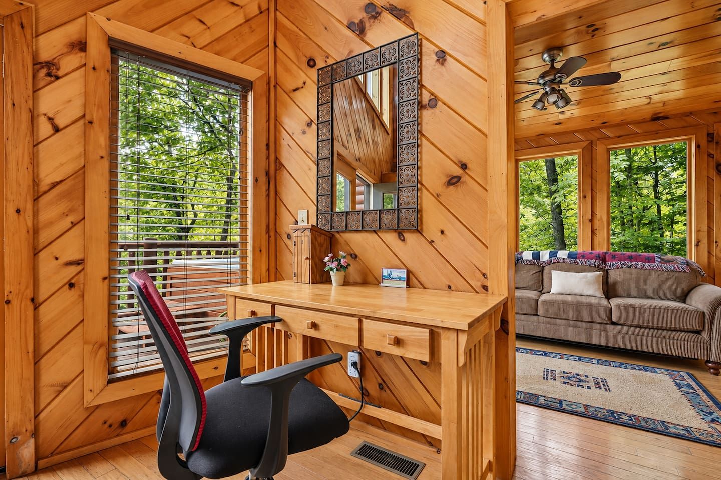 Interior de una cabaña de madera con escritorio, silla y sofá.