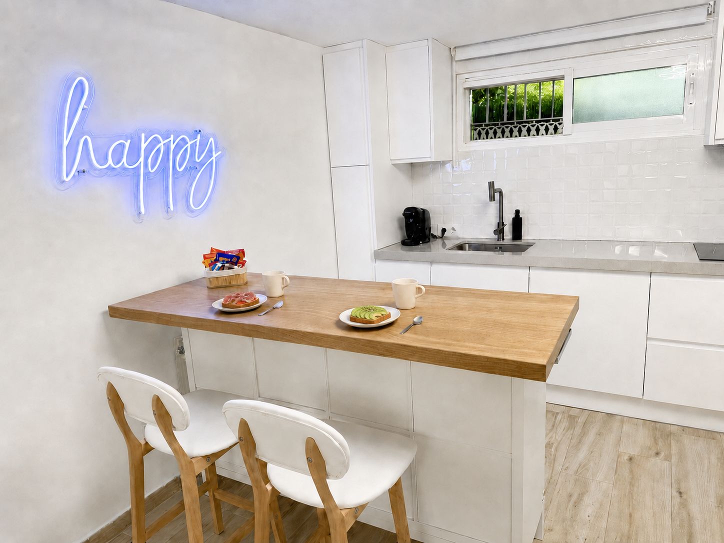 A modern kitchen with a neon sign, a breakfast bar, white cabinets, and a window with a view.