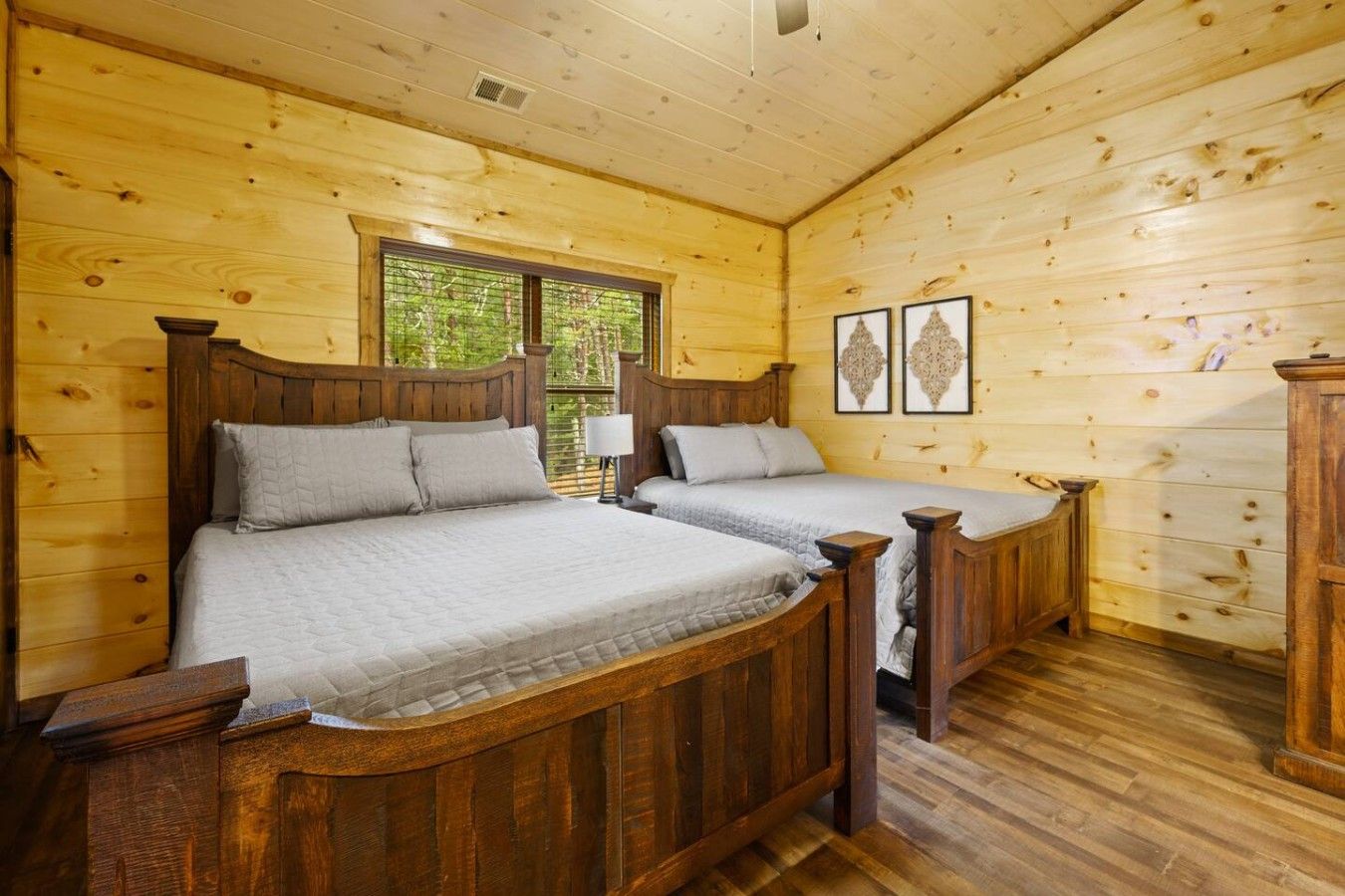 Un dormitorio de cabaña de madera con dos camas, una ventana y obras de arte enmarcadas en la pared.