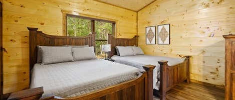 Un dormitorio de cabaña de madera con dos camas, una ventana y obras de arte enmarcadas en la pared.