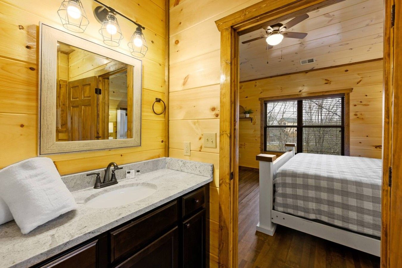A wooden cabin interior with a bathroom featuring a sink, mirror, and towel.