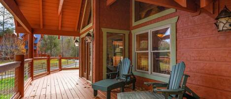 A wooden deck with Adirondack chairs and a covered porch area.