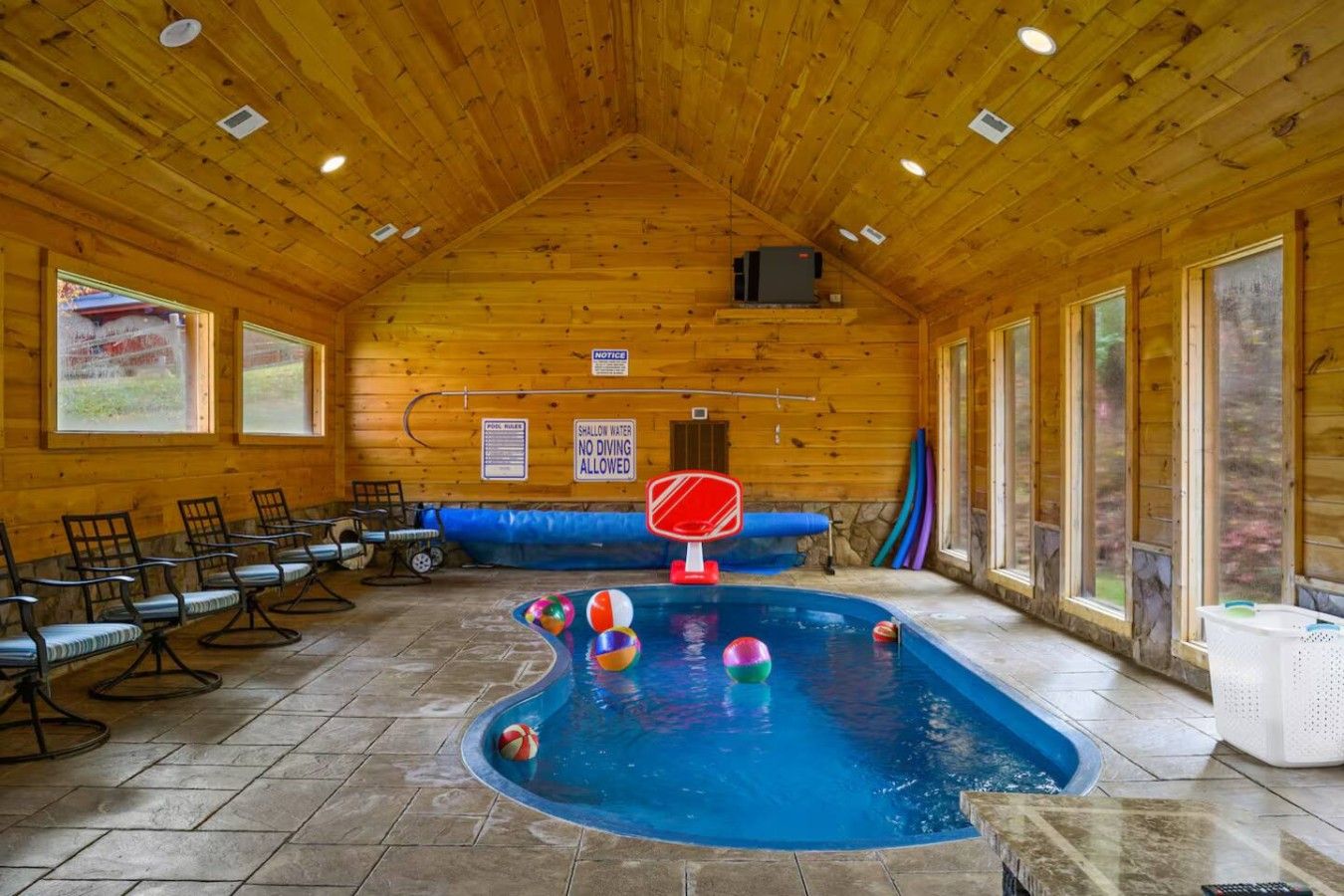 En indendørs swimmingpool med træpaneler, omgivet af stole og en seddel om lavt vand.