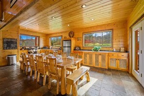 Een houten lodge met een eethoek, keuken en grote ramen met uitzicht op de natuur.