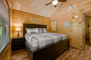 A wooden-paneled bedroom with a bed, nightstands, a ceiling fan, and a window with blinds. - 4BR Pool Cabin w/Hot Tub*Fire Pit*Games*Privacy! (Sevierville)