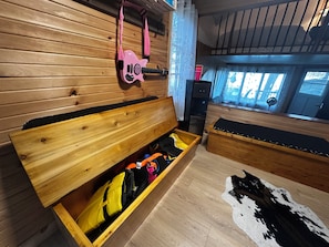 A wooden interior with a bench, a guitar, and a storage box containing bags.