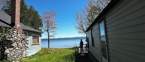 Una cabaña con pared de piedra, terraza de madera y vista al lago.