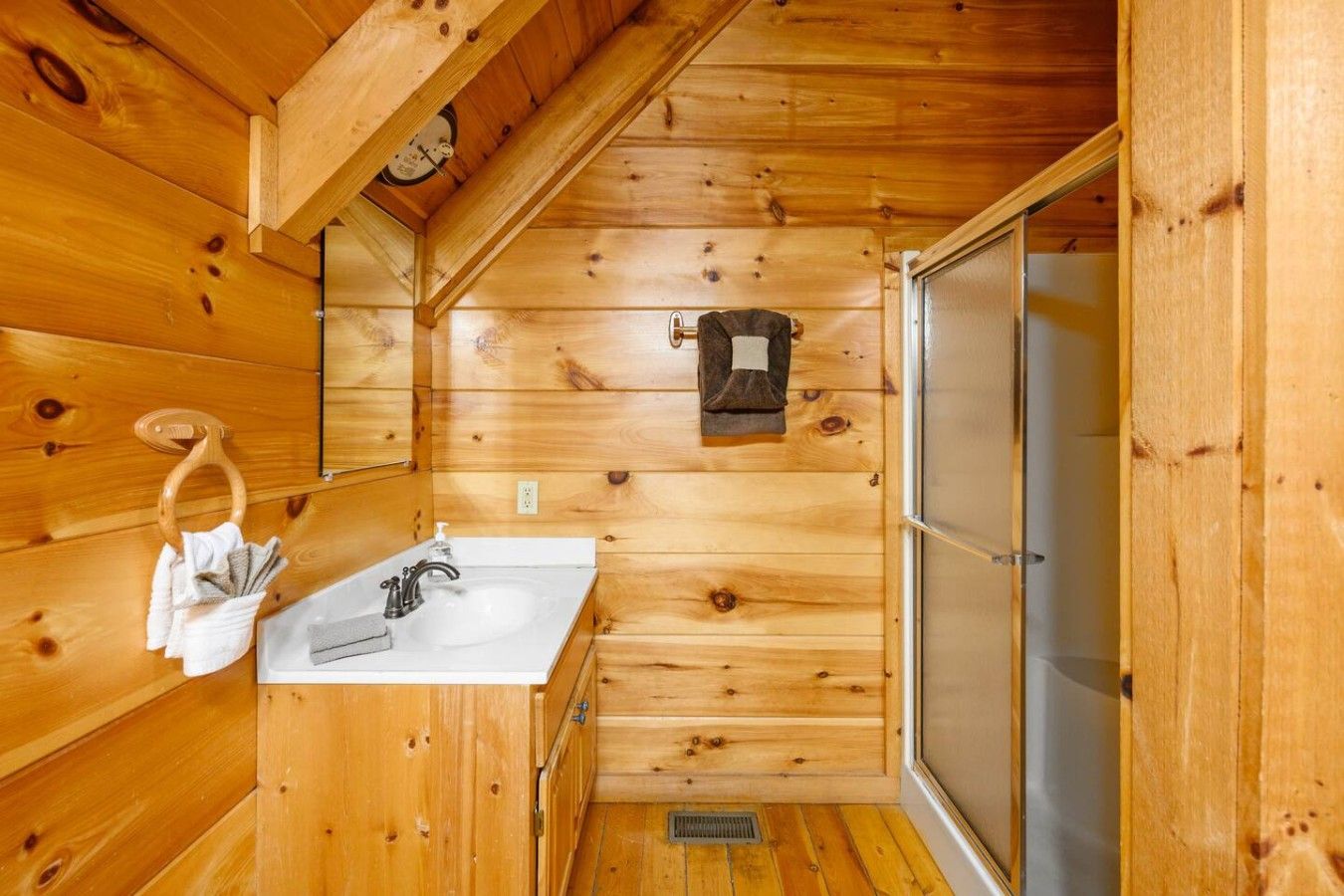 Een houten badkamer in een vakantiehuisje, met een wastafel, handdoekhouder en een klein raam.
