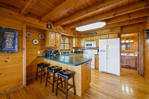 A wooden cabin interior with a kitchen area featuring a refrigerator, microwave, and bar stools. - Incredible MTN Views! Hot Tub*Game Room*Quiet*Pets (Sevierville)