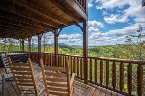Um deck de madeira com banheira de hidromassagem e área de estar com vista para uma paisagem arborizada.