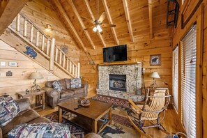 A log cabin interior with a stone fireplace, wooden staircase, and a cozy seating area. - Incredible MTN Views! Hot Tub*Game Room*Quiet*Pets (Sevierville)