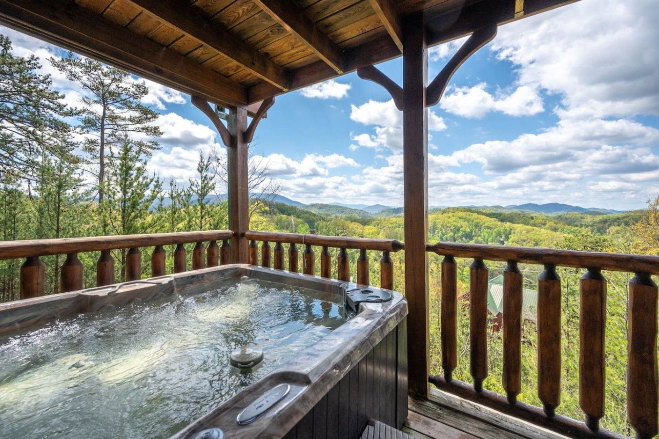 A hot tub on a wooden deck with a view of a forest and mountains.