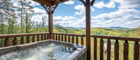 Un bain à remous sur une terrasse en bois, avec vue sur une forêt et des montagnes.