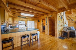A wooden cabin interior with a kitchen, bar stools, a dining area, and a staircase. - Incredible MTN Views! Hot Tub*Game Room*Quiet*Pets (Sevierville)