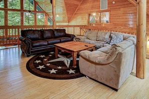 Ein gemütliches Interieur mit Holzboden, einem Ledersofa, einem beigen Sessel und einem Teppich mit Sternenmuster.