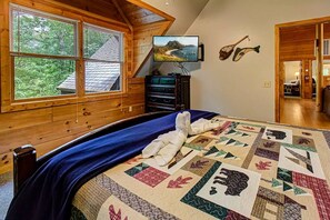 Ein Schlafzimmer mit einem großen Bett, einem Fernseher an der Wand und Blick ins Freie durch das Fenster.