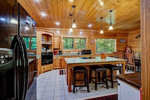 A wooden cabin kitchen with a central island, built-in appliances, and large windows. - 5 King Suites! Hot Tub*Game Room*Quiet*Privacy! (Gatlinburg)