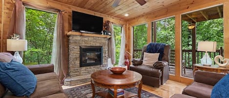 Una sala de estar acogedora con chimenea de piedra, techo de madera y ventanas amplias.