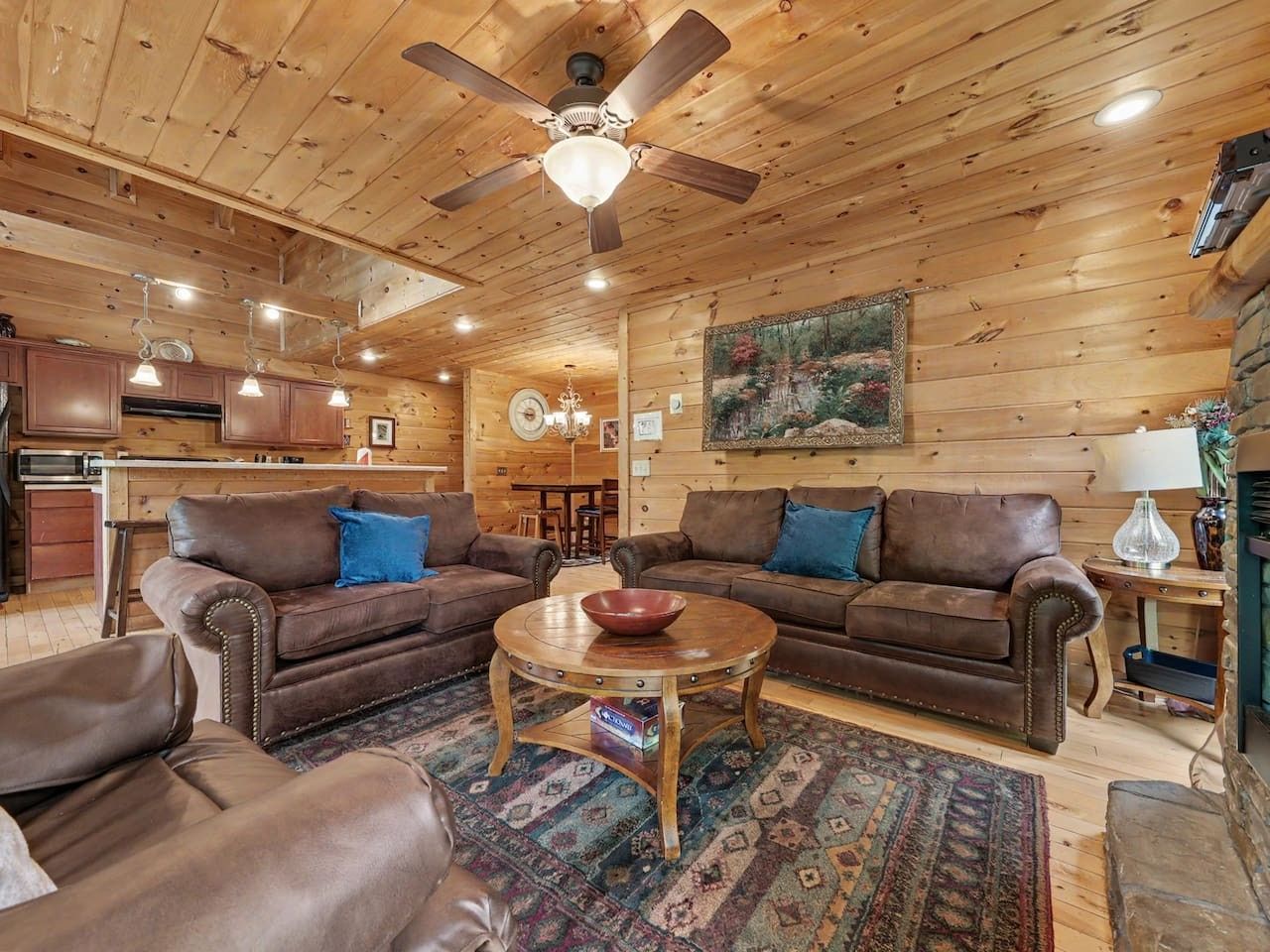 A cozy cabin interior with two leather sofas, a coffee table, and a dining area.