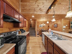 A wooden interior with a kitchen featuring a stove, oven, and modern appliances. - Peaceful 3BR w/Hot Tub*Theater*Game Room*Privacy! (Sevierville)
