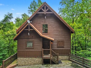 A wooden cabin with a stone foundation, a wooden porch, and a satellite dish. - Peaceful 3BR w/Hot Tub*Theater*Game Room*Privacy! (Sevierville)