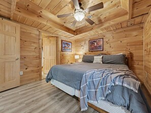A wooden cabin bedroom with a bed, a ceiling fan, and two wall-mounted pictures. - Peaceful 3BR w/Hot Tub*Theater*Game Room*Privacy! (Sevierville)