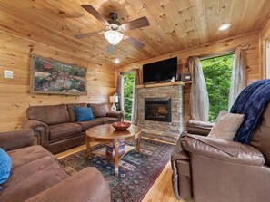 A cozy cabin interior with a fireplace, wooden walls, and a ceiling fan. - Peaceful 3BR w/Hot Tub*Theater*Game Room*Privacy! (Sevierville)