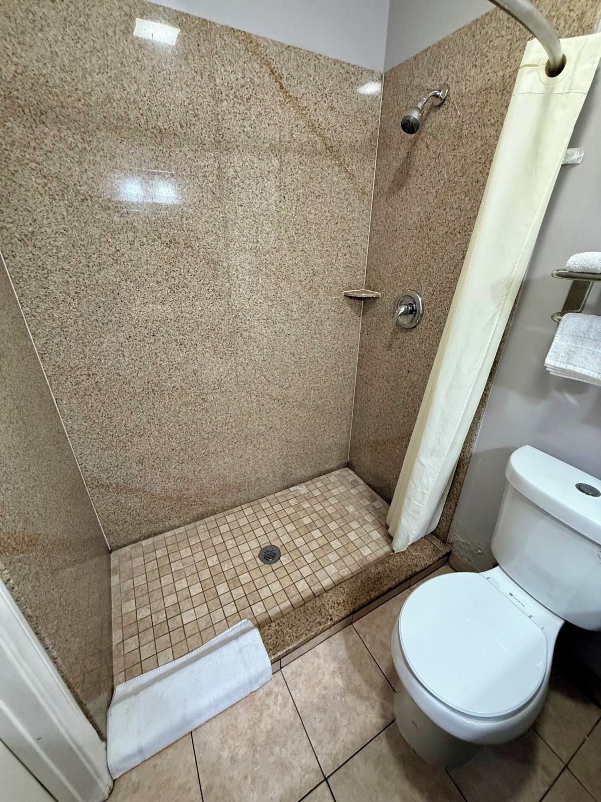 Ein Badezimmer mit Dusche, Toilette und Fliesenboden.