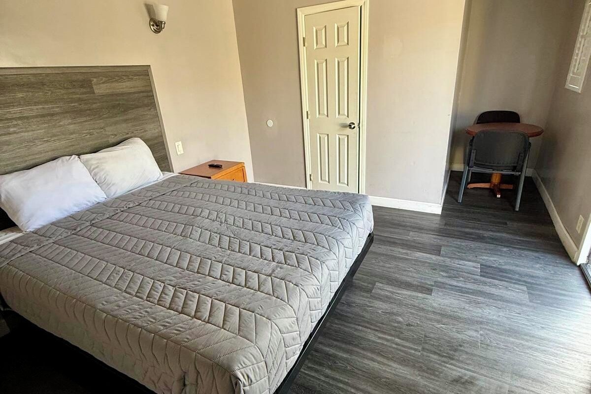 A bedroom with a bed, a door, a chair, and a small table.