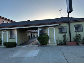 Un edificio de dos pisos con techo plano, entrada visible y un pequeño jardín frontal.