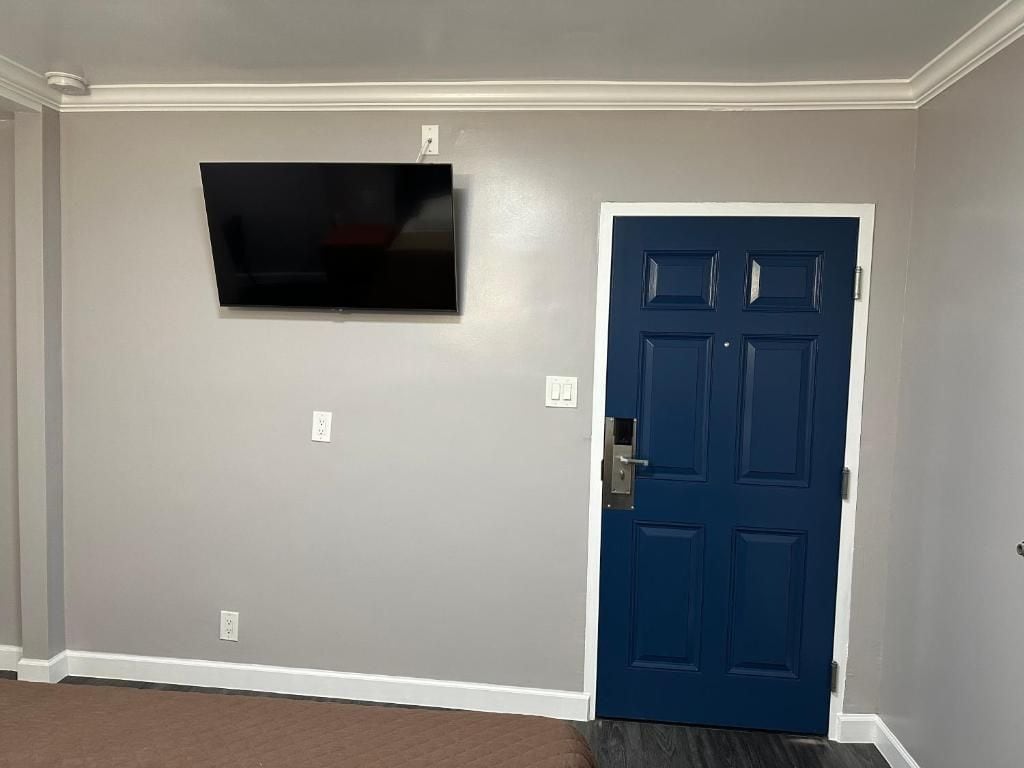 Una habitación con televisión de pantalla plana montada en la pared, una puerta azul y suelo alfombrado.