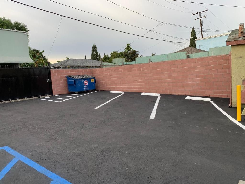 A parking lot with marked parking spaces, a blue dumpster, and a brick wall.