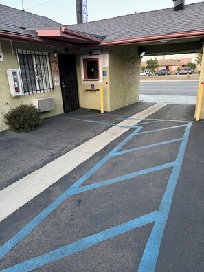 A building with a red awning, a black door, and a window with a metal grill. There is a blue parking space with diagonal lines.