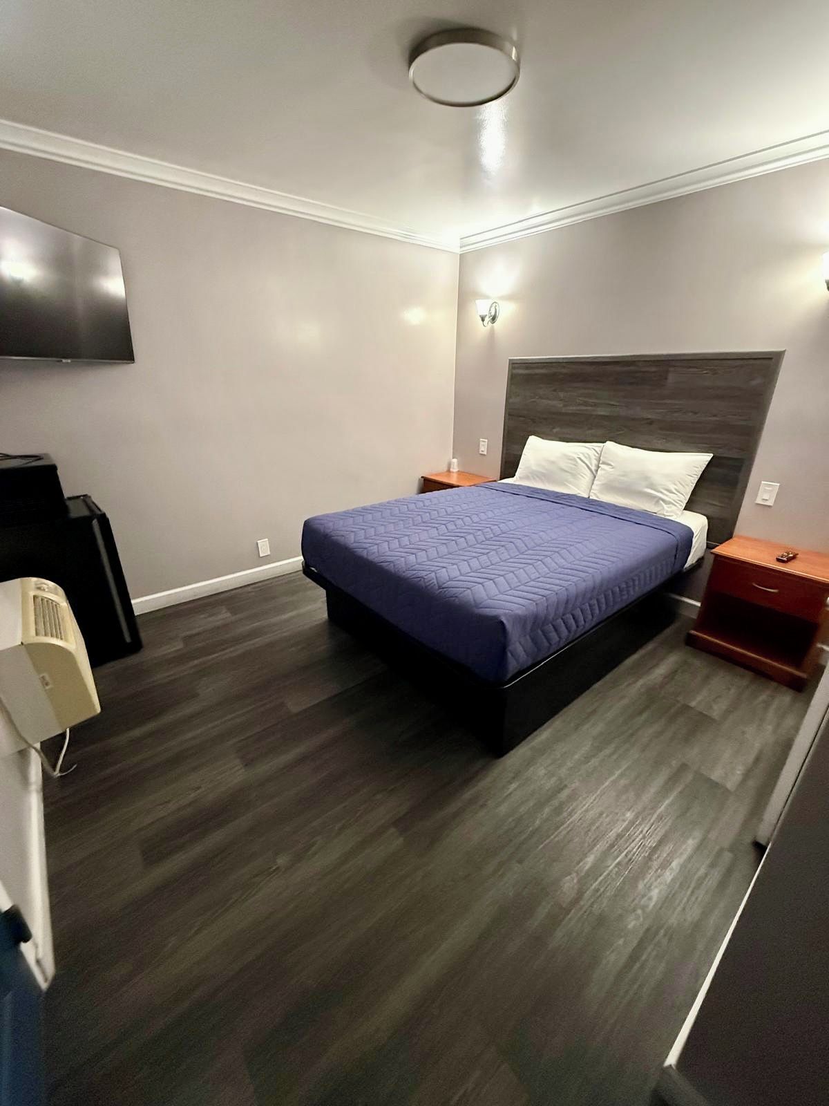 Habitación de hotel moderna con una cama grande, televisión de pantalla plana, mesita de noche y calefacción integrada.