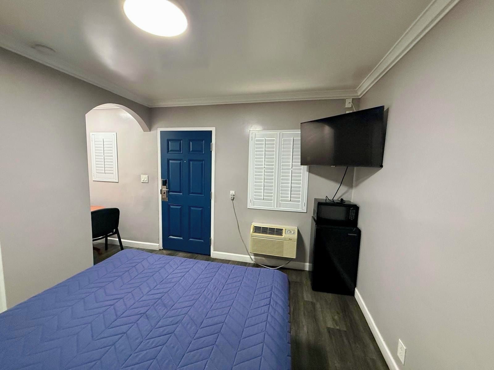 Un dormitorio con cama, televisor, puerta y ventana con contraventanas.