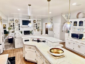 A spacious kitchen with a marble island, white cabinetry, and pendant lighting.