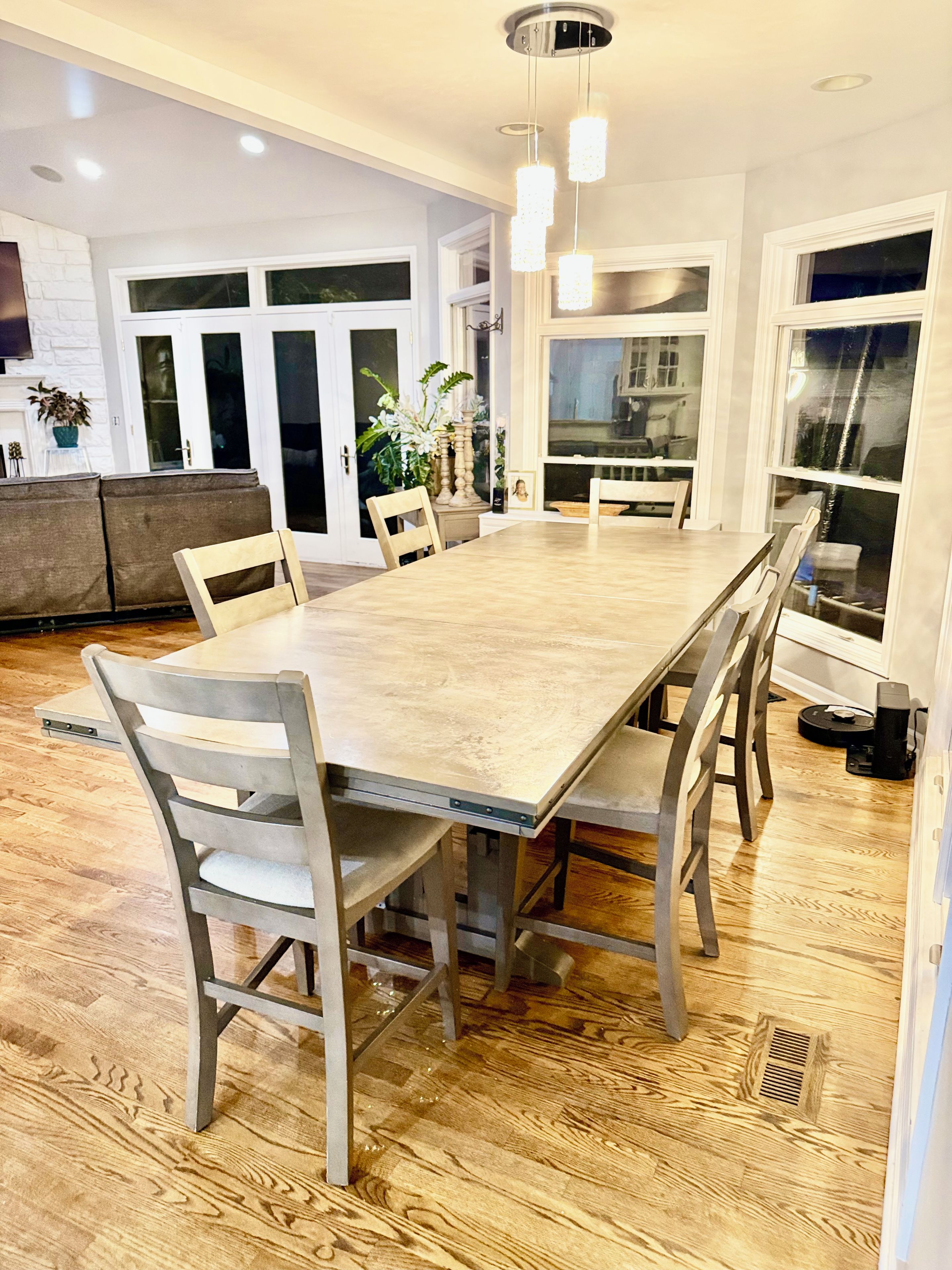 Uma sala de jantar com uma grande mesa de madeira, seis cadeiras e iluminação pendente.