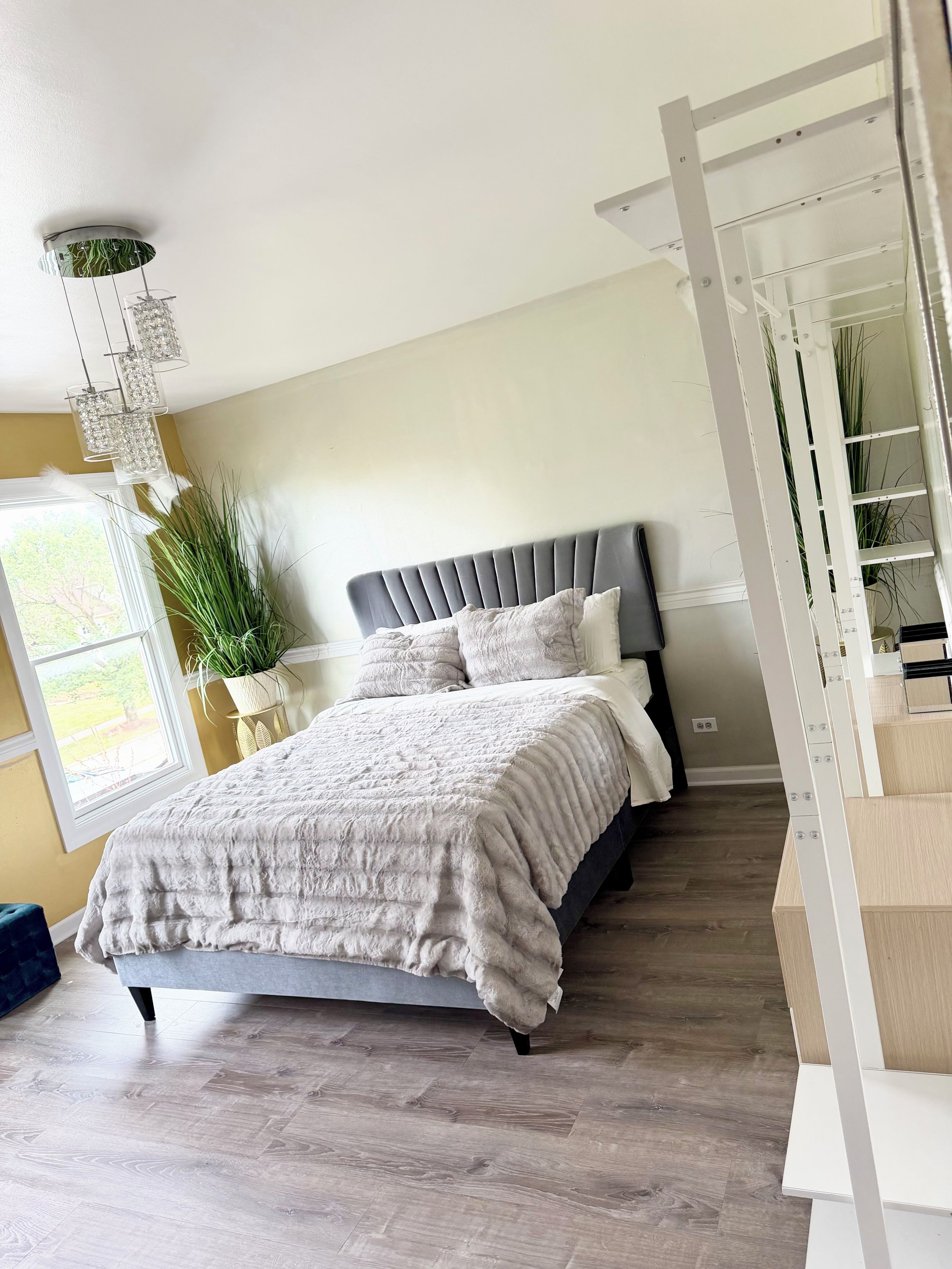 A bedroom with a bed, a potted plant, and a staircase.