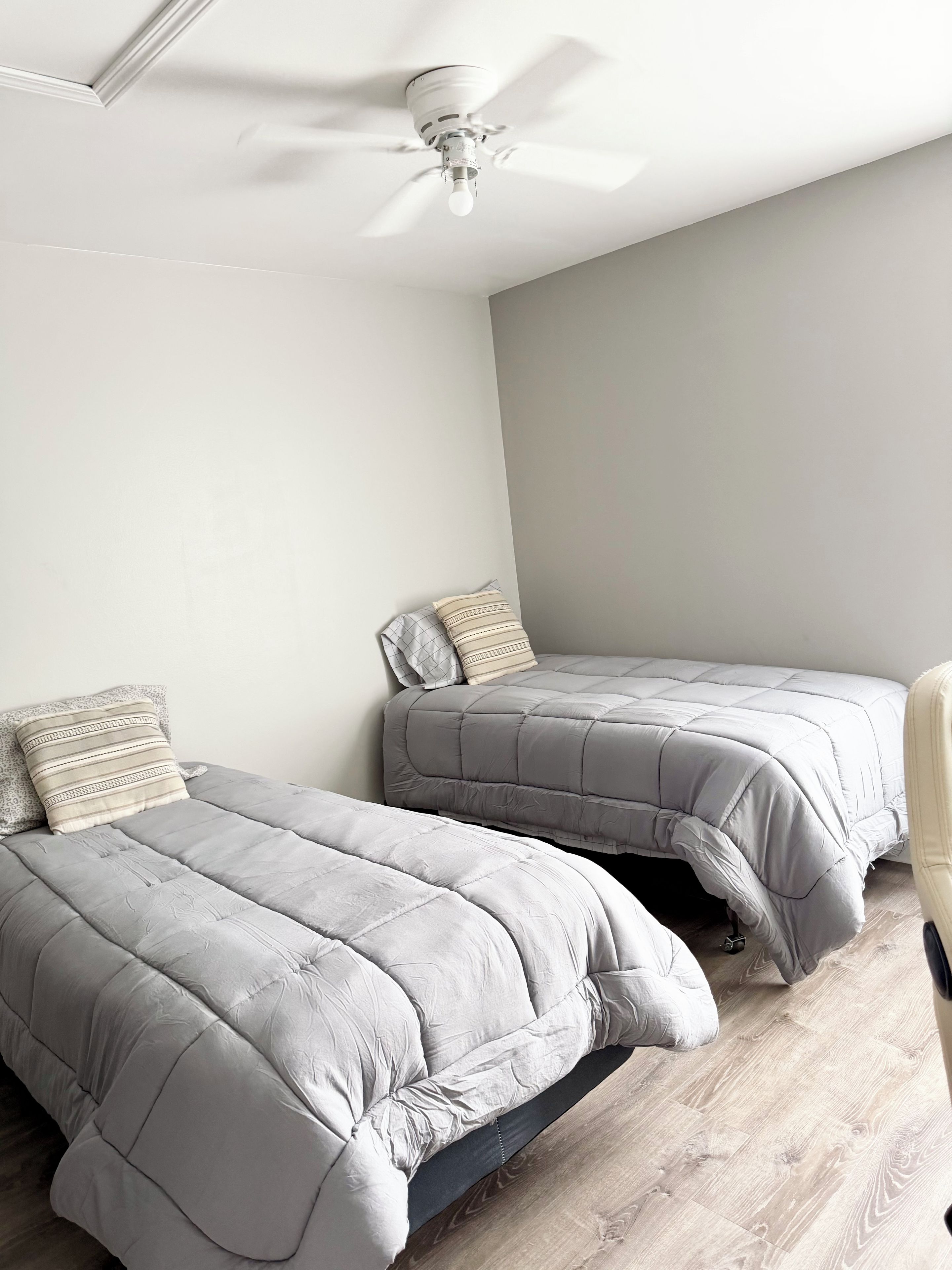 Une chambre avec deux lits, un ventilateur de plafond et un plancher en bois.