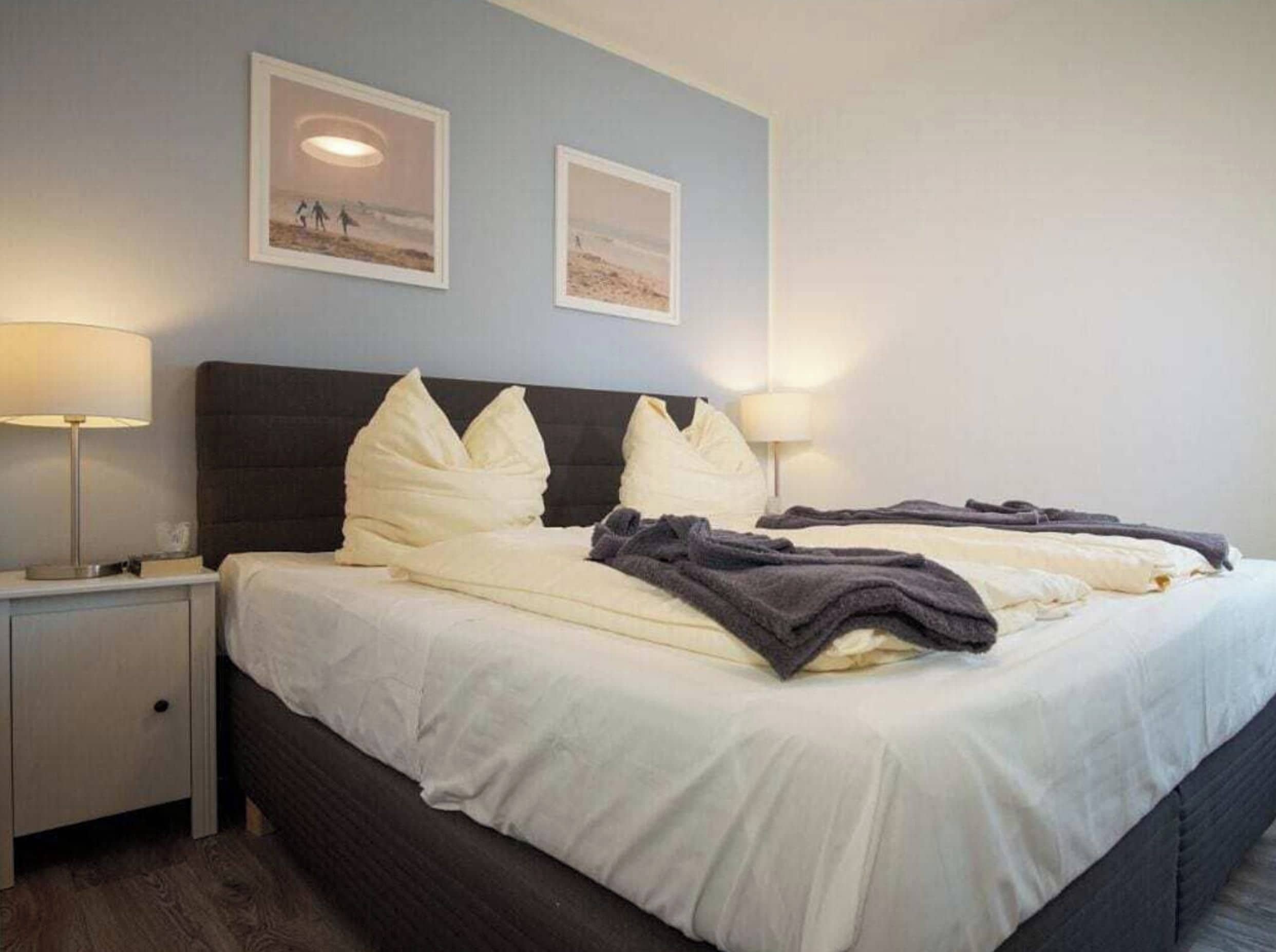 A hotel room with a bed, two bedside lamps, and two framed pictures on the wall.