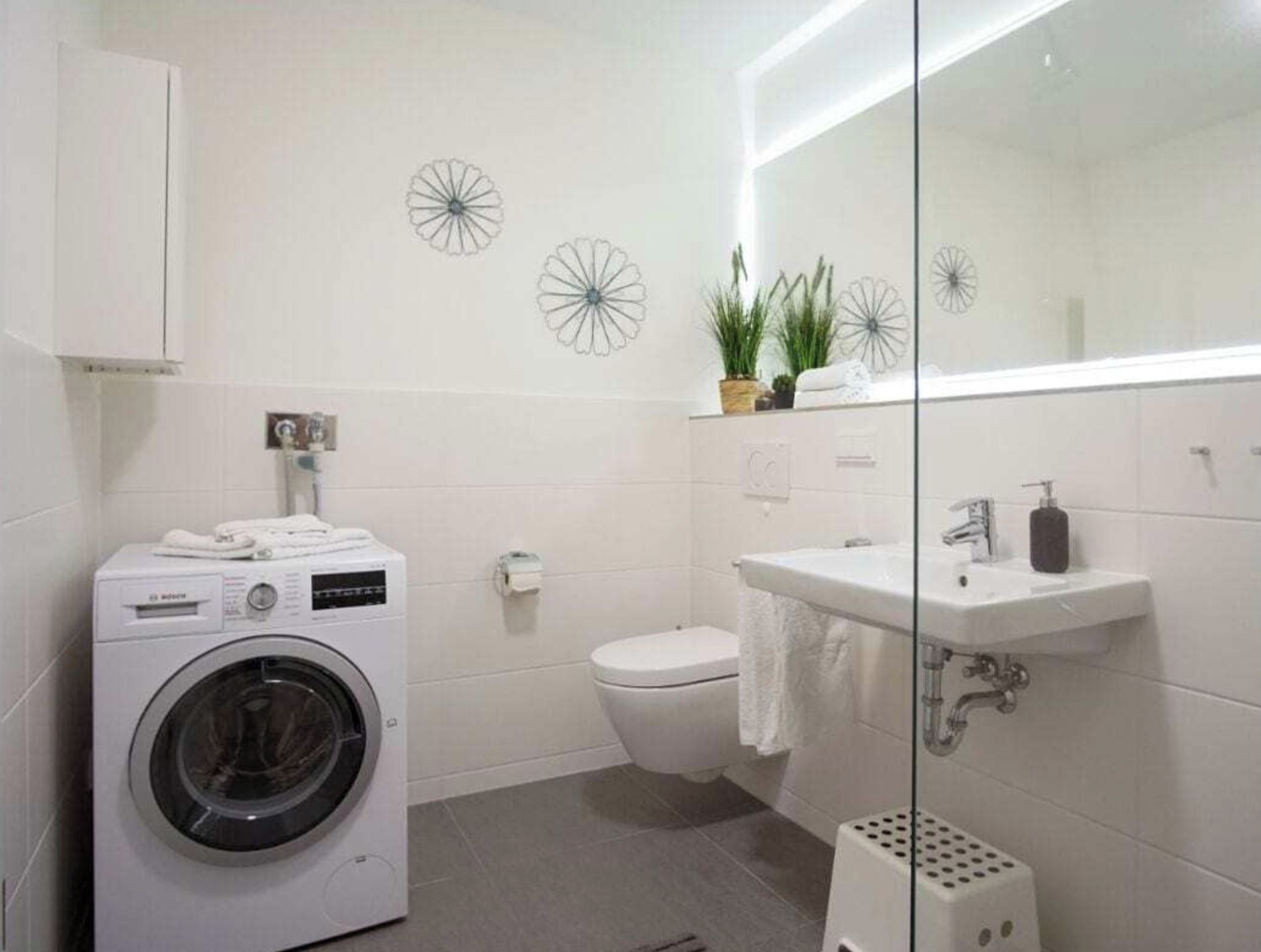 Un baño moderno con lavadora, inodoro, lavabo y decoración en la pared.