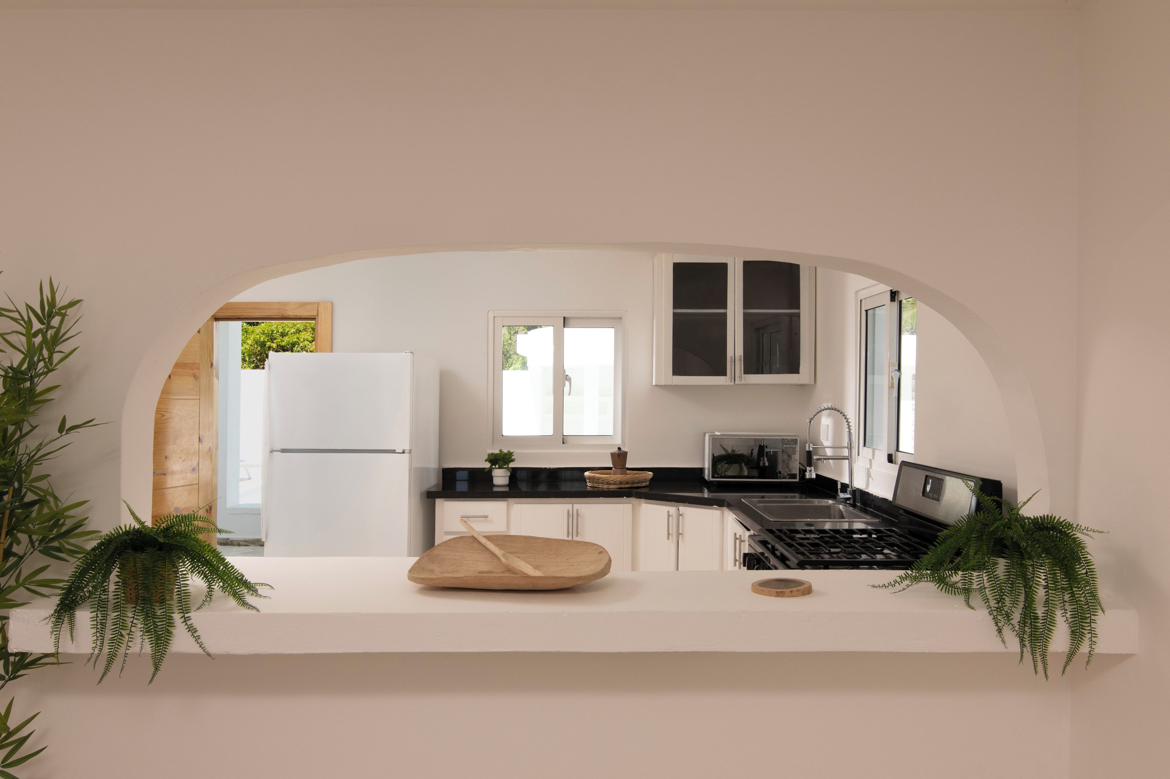 A modern kitchen with white cabinetry, a black countertop, and a central island with a wooden cutting board and a wooden spoon.