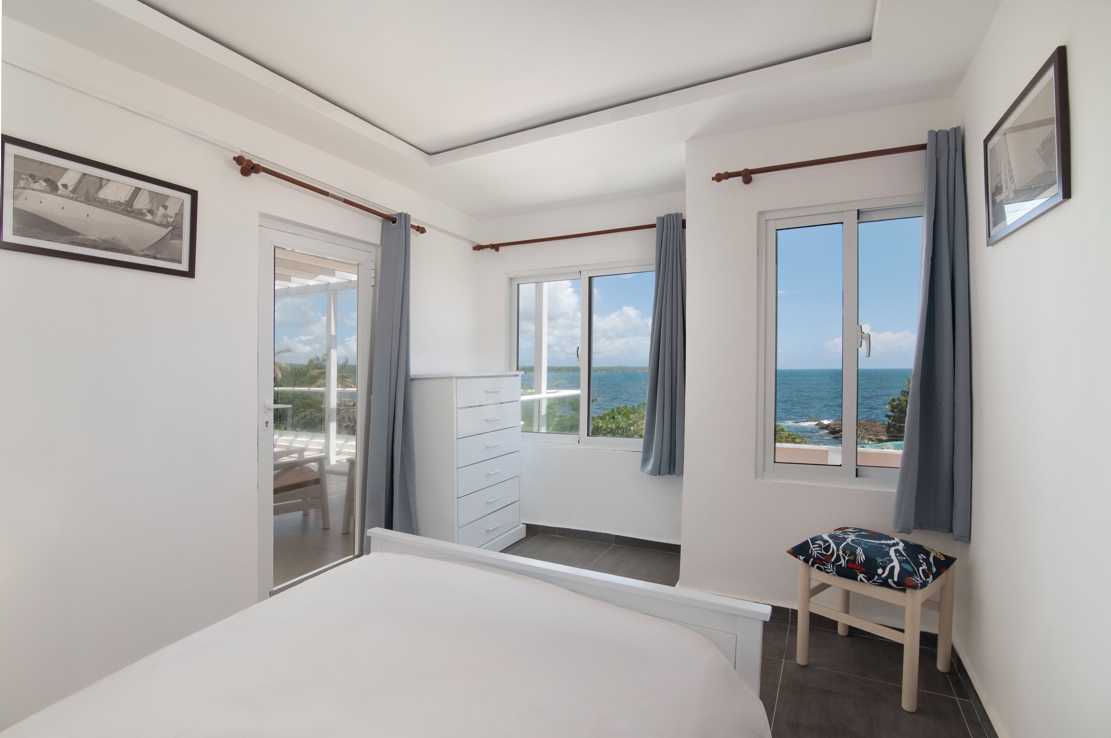 Une chambre avec un grand lit, une commode, une chaise et une vue sur la mer.