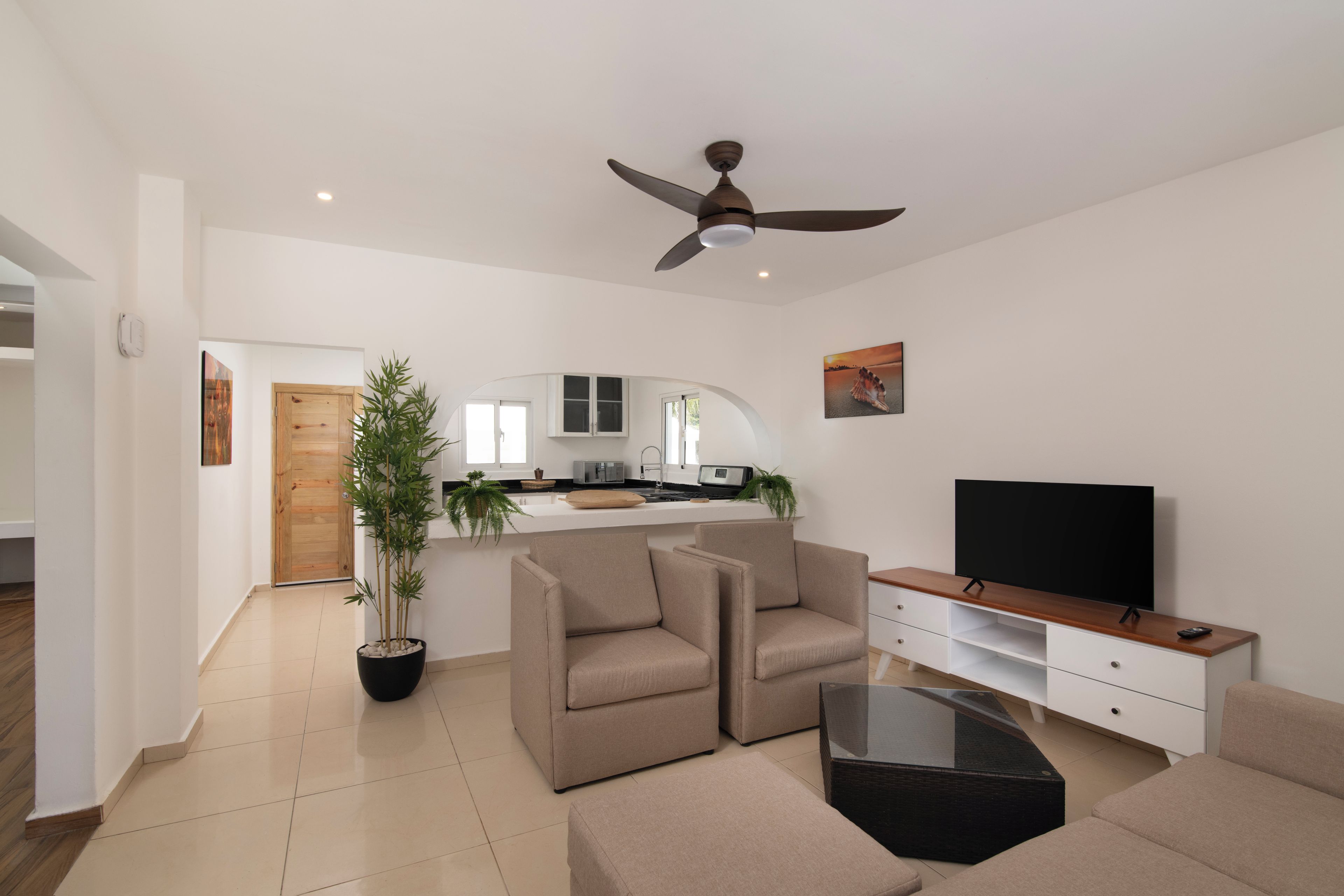 Een moderne woonkamer met een flatscreen televisie, beige banken, een glazen salontafel en een plafondventilator.